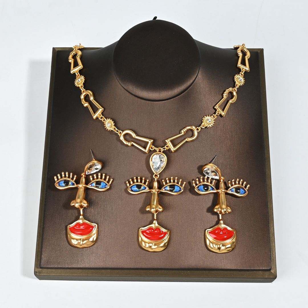 Surrealist Muse 18K gold plated jewelry set displayed on mannequin bust, anatomical eye earrings and crimson lip necklace