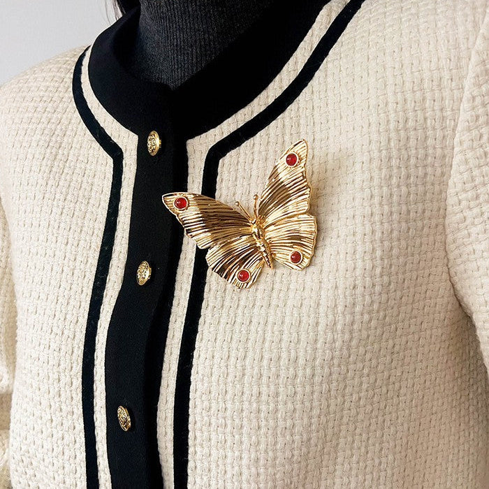 Lifestyle shot of the gold textured butterfly brooch pinned on a cream-colored knit cardigan, demonstrating its size as a statement accessory.