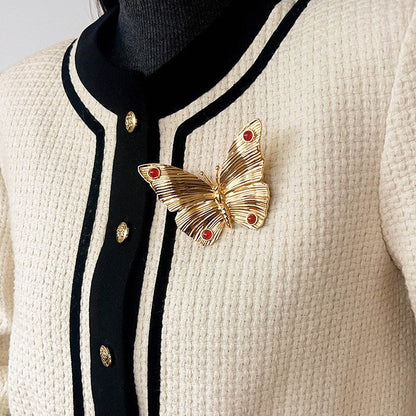 Lifestyle shot of the gold textured butterfly brooch pinned on a cream-colored knit cardigan, demonstrating its size as a statement accessory.
