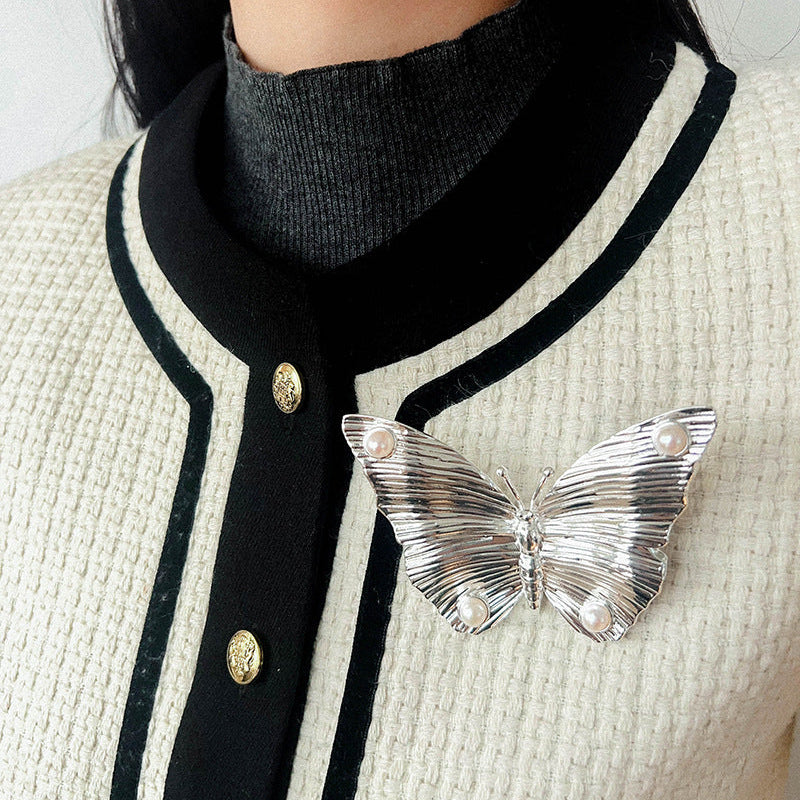 A model wearing the silver butterfly brooch on a classic white and black trim cardigan, showing how it adds a vintage touch to modern knitwear.