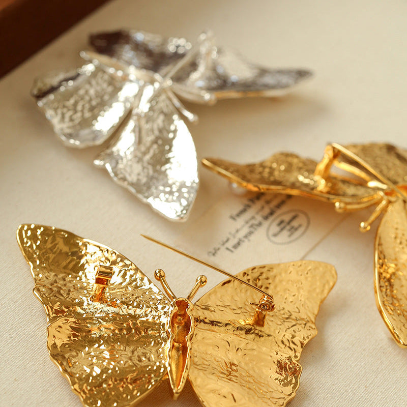 Detailed flat lay of the butterfly brooches with vintage paper, emphasizing the brand's aesthetic of "museum-quality" cultural jewelry.