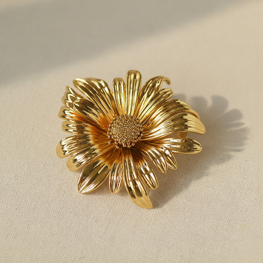 Close-up of a large gold-toned chrysanthemum brooch with a matte metallic texture, showcasing a 3D sculptural floral design.