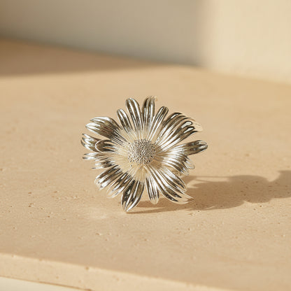 Side view of a silver metallic sun-ray flower brooch on a neutral background, highlighting the depth and elegant curvature of the petals.
