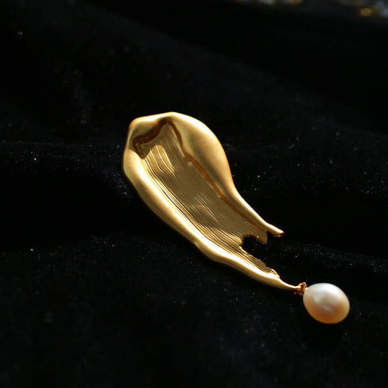Detailed close-up of the molten, fluid gold-toned metal brooch against a rich black velvet background, emphasizing the unique organic form and natural luster of the pearl.