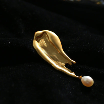 Detailed close-up of the molten, fluid gold-toned metal brooch against a rich black velvet background, emphasizing the unique organic form and natural luster of the pearl.