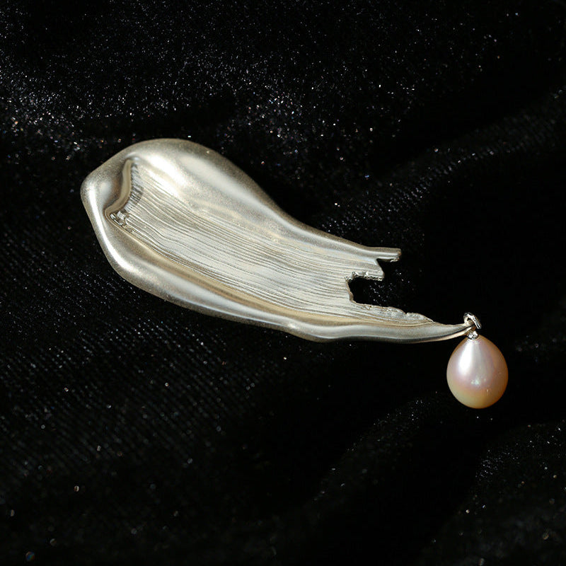 A textured, sculptural silver-toned brush-stroke brooch on black velvet, showing the refined, imperfect metallic surface and a solitary hanging baroque pearl.