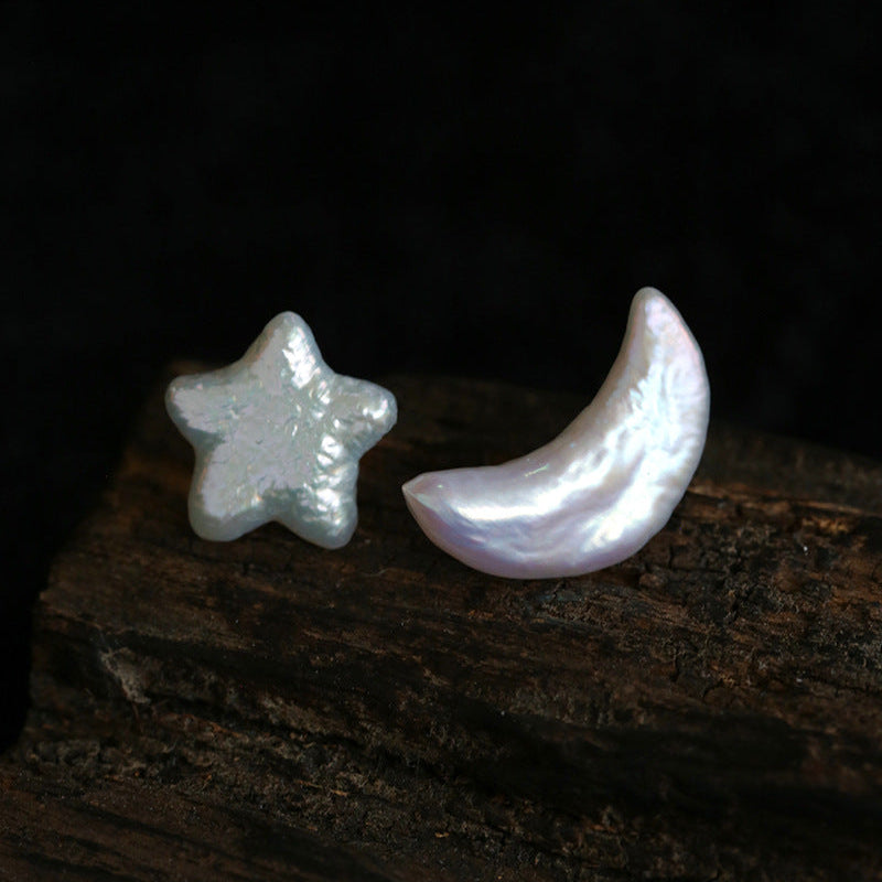 Mismatched star and moon baroque pearl stud earrings set in silver, asymmetrical celestial earrings for women, flat lay on white background