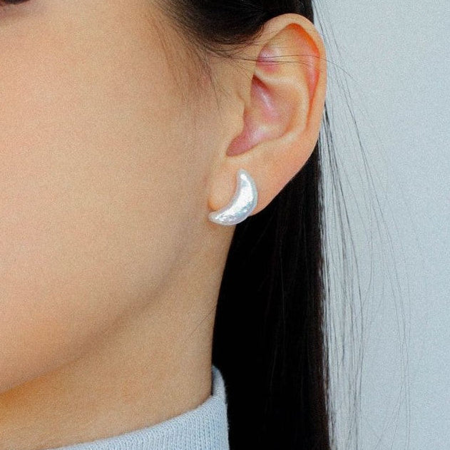 Close-up of model wearing crescent moon baroque pearl stud earrings in silver, natural iridescent pearl, dainty celestial jewelry on ear