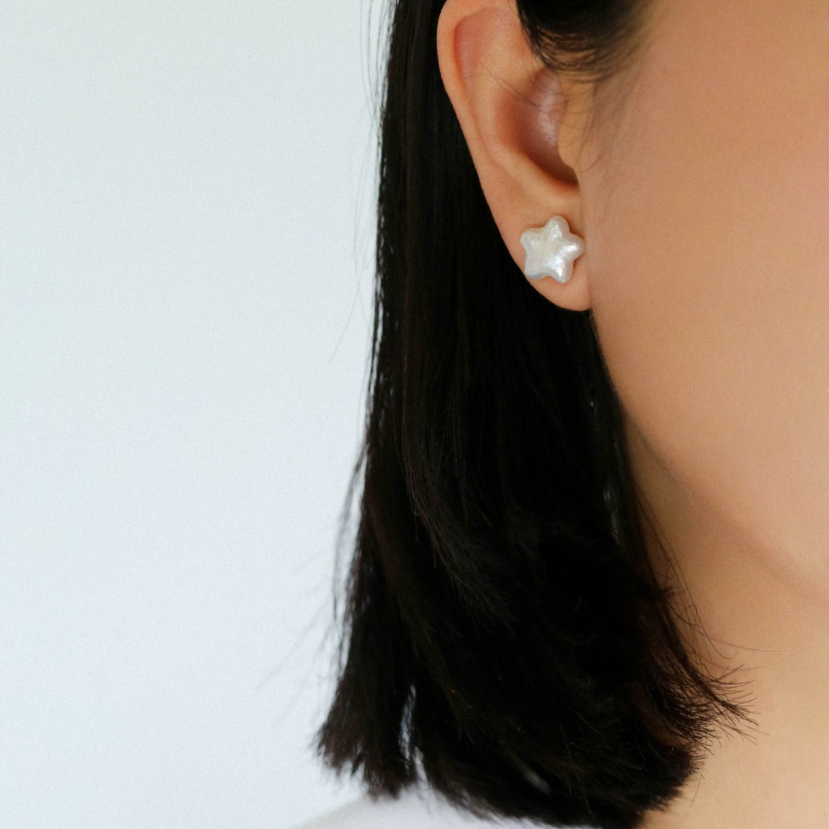 Woman wearing star-shaped baroque freshwater pearl stud earrings in S925 silver, close-up ear shot, minimalist celestial jewelry styled look

