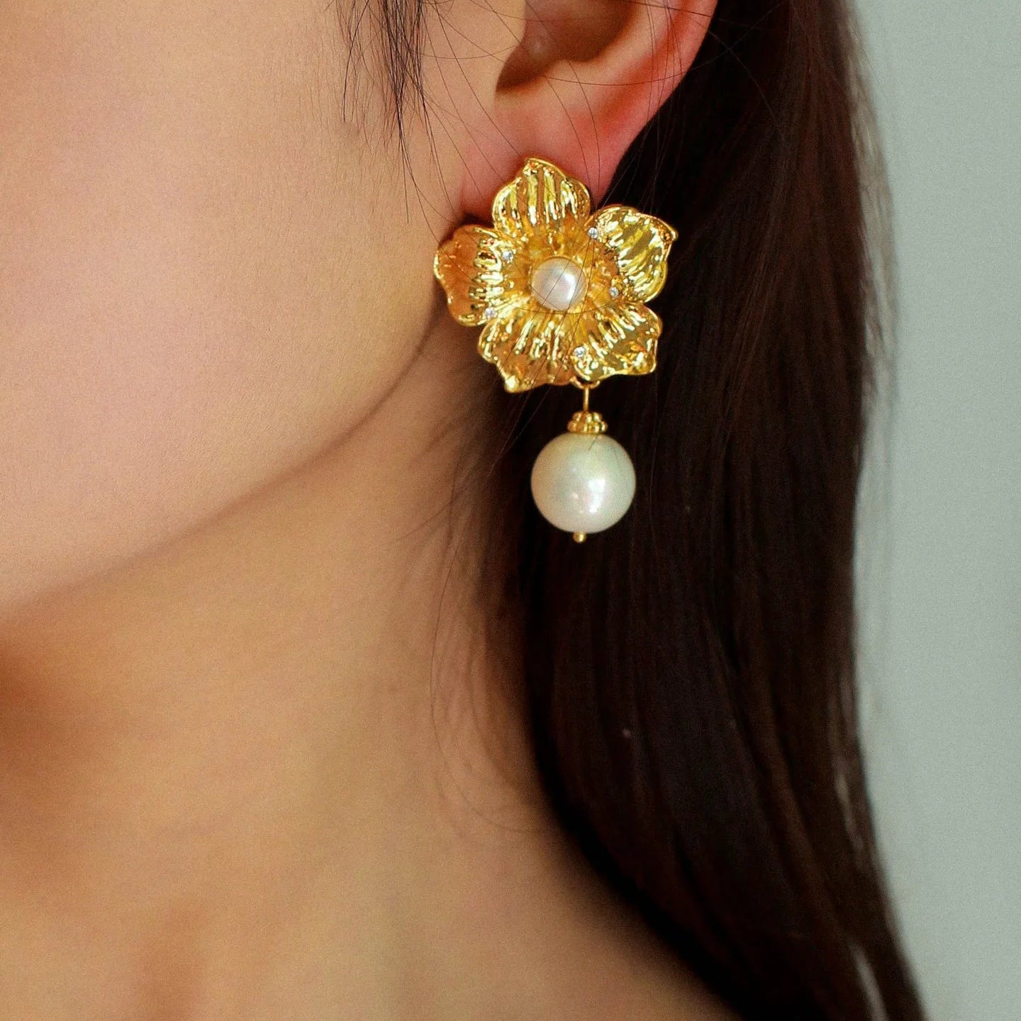 Model wearing elegant gold flower and pearl earrings, close-up side view.