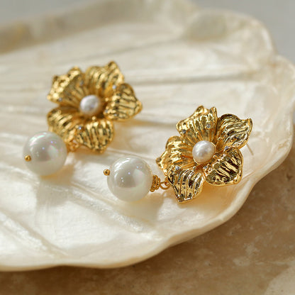 Handcrafted gold floral pearl earrings resting on a decorative shell tray.