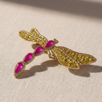 Macro shot of the vintage-inspired dragonfly pin, highlighting the brilliant sparkle of the premium yellow crystals and the smooth, matte luster of the gold-plated finish under warm sunlight.