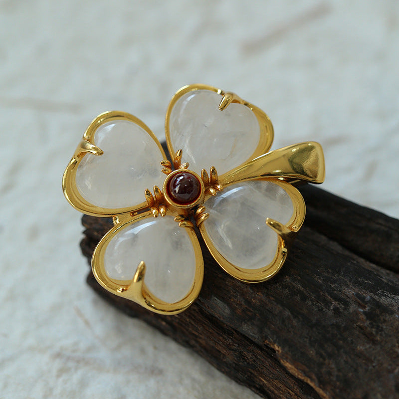 A detailed view of the four-leaf clover inspired brooch on a piece of dark aged wood, highlighting the semi-translucent quality of the petals and the intricate gold hardware.