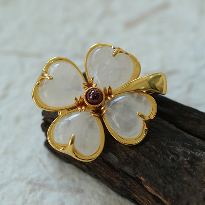 A detailed view of the four-leaf clover inspired brooch on a piece of dark aged wood, highlighting the semi-translucent quality of the petals and the intricate gold hardware.