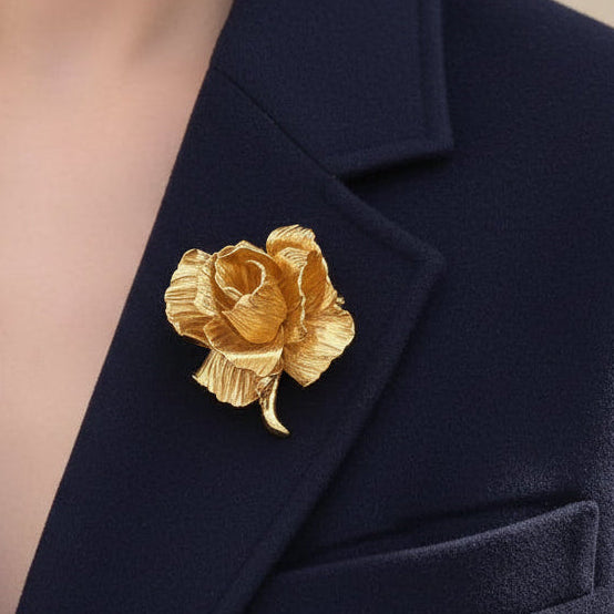 Model wearing a bold gold rose statement brooch on a navy blue blazer lapel.