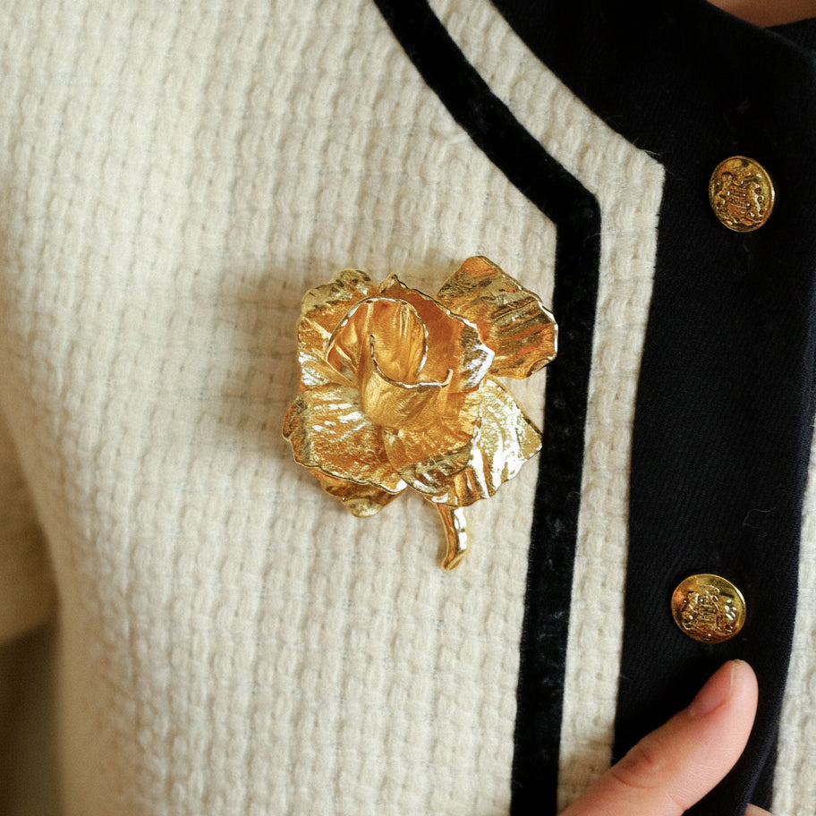 Model wearing a bold gold rose statement brooch on a White blazer lapel.