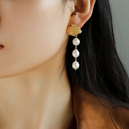 Model wearing triple baroque pearl dangle earrings in 18K gold lava texture, styled for evening wear