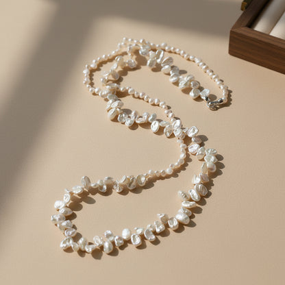 Luxurious double-strand baroque pearl necklace with irregular keshi pearls, displayed on a warm beige surface with elegant architectural shadows.