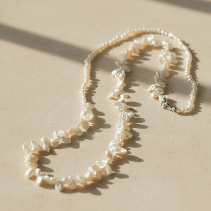 Overhead flat lay of the irregular pearl necklace on a warm-toned background, showing the full arrangement of the two distinct strands.