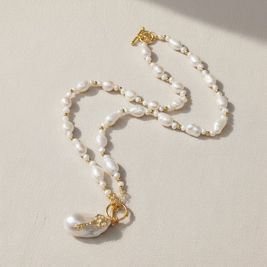 Elegant baroque pearl necklace featuring a unique gold vintage key pendant and irregular pearls, displayed on a warm neutral-toned surface.