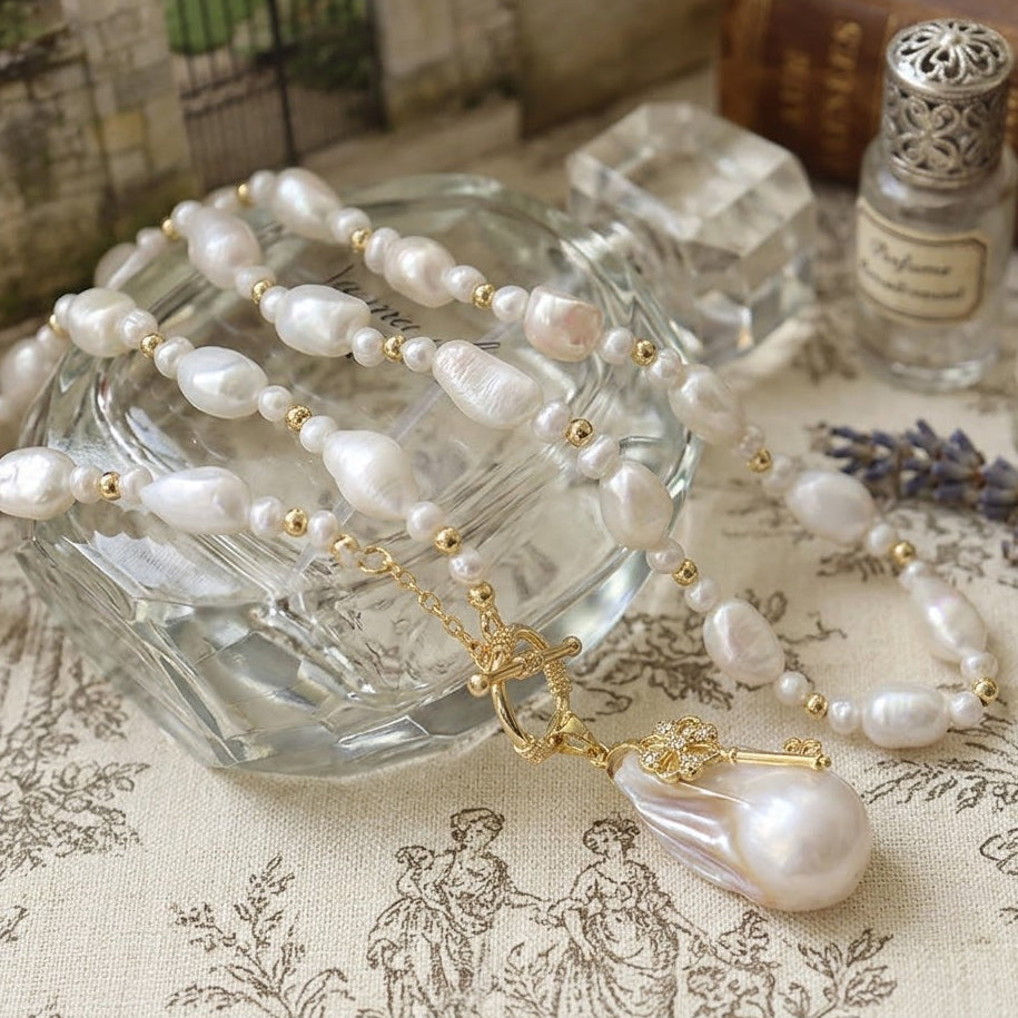 Close-up of the gold key charm paired with textured baroque pearls draped over a glass, highlighting the intricate vintage design.