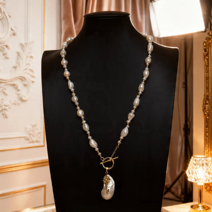The long baroque pearl necklace with a statement key pendant displayed on a black jewelry bust, showing its full length and artistic drape.