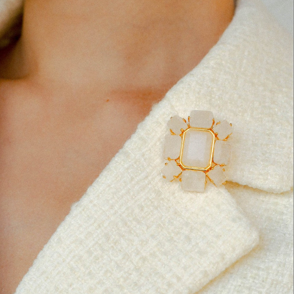 Geometric white quartz pin styled on a cream tweed blazer lapel, timeless accessory for professional women's workwear.