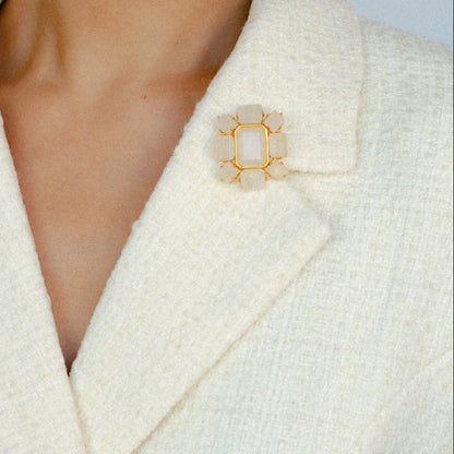 Modern rock crystal lapel pin on a white structured wool coat, minimalist centerpiece for luxury winter fashion.