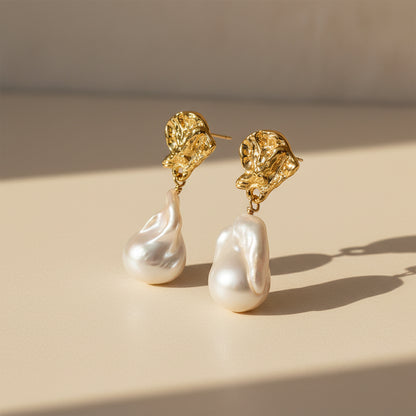 Baroque pearl drop earrings standing upright on beige stone background showing sculptural lava texture 18K gold plated

