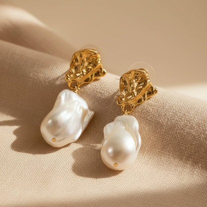 Close-up detail of baroque pearl drop earrings organic lava texture on beige fabric background 18K gold plated brass

