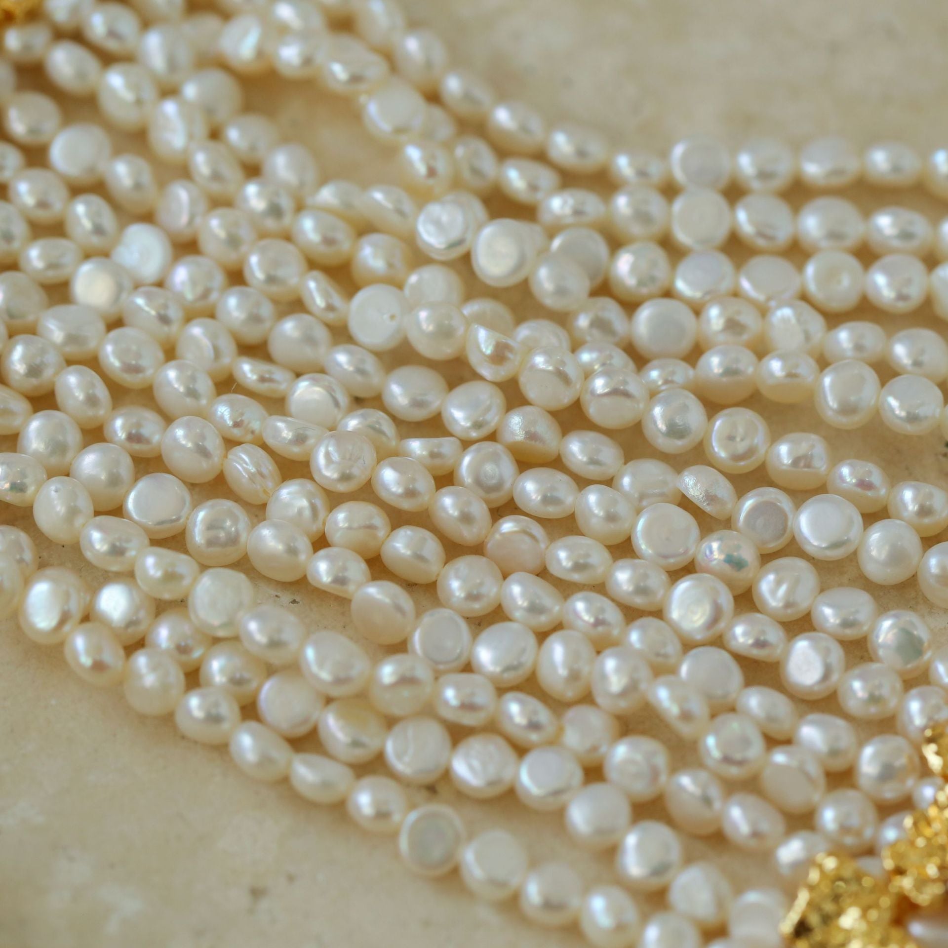 Close-up detail of multi-strand mini freshwater pearl choker on beige background 18K gold plated brass clasp and pearl texture

